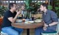 Two men sitting talking at a restaurant table, with plants next to them