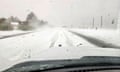 The view of a snow-covered road from the front windshield of a car in motion