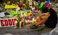 A person sits with their head in their arms next to a makeshift memorial of handmade signs and candles