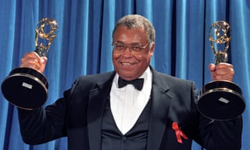 man wearing black suit, bowtie and glasses holds two gold statues