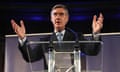 Jacob Rees-Mogg raises both hands as he speaks behind a lectern