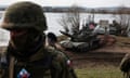 a soldier stands near a tank by a body of water