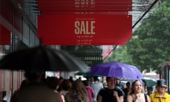 Shoppers with umbrellas walking along a street lined with stores