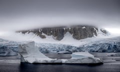 A iceberg floats in front of Antarctic land ice and a looming misty mountain