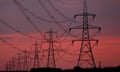 A hazy, pink and purple sunrise behind electricity pylons in the countryside