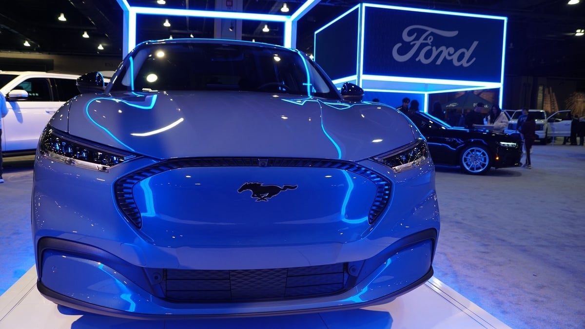 Blue Ford Mustang Mach-E GT electric SUV in a Ford showroom with Ford sign and logo in background.