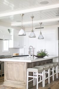 White kitchen design with light wooden cabinets; sink in island with cabinets on both sides