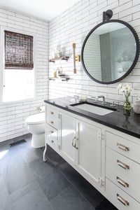 Slate on the floor with a white furniture style vanity with a black quartz countertop + round black mirror + white subway tile covering the whole bathroom | Lucy and Company