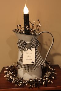 "A tall white pitcher candelabra light with black and white pip berries around the base of the light and a wired black and white checked wired bow with a hang tag that says \"Bless This Home\" tied around the handle.   The pitcher measures 16\" tall (with bulb) x 8\" wide (with spout and handle) x 6\" deep.  The berry ring around the base measures approximate 8 inches around the outside.  It includes a low wattage silicone bulb.  The 4 1/2 foot cord has a roller switch on it.  The candelabra lig