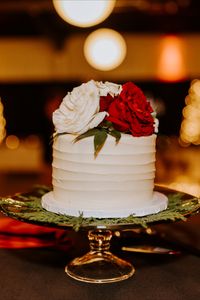 Simple, single tier white wedding cake topped with blooms of white and red roses with Italian ruscus and cedar greenery for a red and white winter wedding at the Kankakee County Fairgrounds in Kankakee, Illinois. Created by J.Blu Design Wedding and Event Florist in Peoria, IL. Photo by Krystal Richmond Photography. www.jbludesign.com