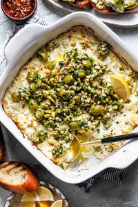 Creamy Baked Feta and Artichoke Dip topped with zippy Olive Gremolata contains all the building blocks of a perfect party dip. Serve hot out of the oven or at room temperature with crostini or pita for the ultimate crowd pleaser. #bakedfeta #thanksgivingappetizers #appetizers #diprecipes