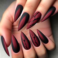 Medium, almond nails painted in a dark, matte blood red. The tips are sharpened to resemble claws. Some nails feature small black cracks or cuts, giving a sinister and dangerous appearance. The nails have a matte finish.