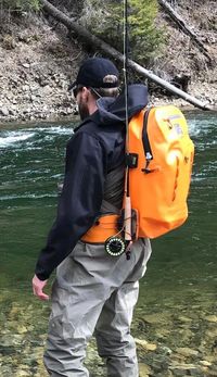 This photo shows a waterproof fishing backpack being worn by a fisherman near a river. #fishinggear