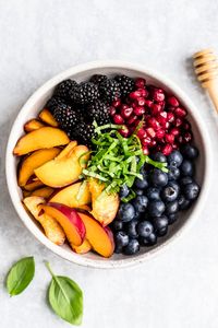 Gorgeous honey lime basil peach fruit salad made with fresh peaches, blackberries, blueberries and pomegranate. This summer peach fruit salad recipe is lightly tossed with honey, lime juice, and fresh basil leaves for a fresh side dish that's perfect for bbq's and parties! #fruitsalad #sidedish #peachrecipe #peaches #blueberries #blackberries