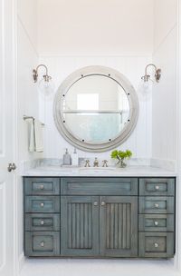 Distressed Bathroom Cabinet. This bathroom features vertical shiplap walls lined with a large gray wood mirror illuminated by clear glass barn sconce over a gray distressed washstand topped with white marble fitted with an oval sink and satin nickel faucet. #Bathroom #Distressed #Cabinet Laura U, Inc.