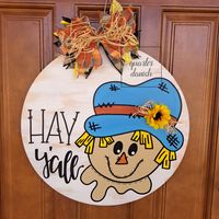 Say "Hay y'all" to your guests with this hand painted scarecrow door hanger. The ribbon and sunflower give this piece the perfect touch of dimension.  Ribbon used in bow may vary based on availability. Colors may appear different based on screen settings. Due to the handmade nature of this sign there will be slight variations from the listing pictures. Color customization welcome as all signs are painted upon order.  To extend the life of your door hanger, do not place in direct sunlight and pro