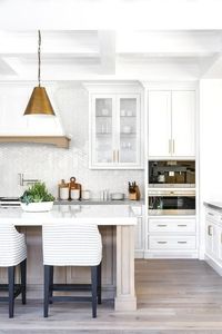 Gray striped upholstered counter stools sit at a gray wash wood island topped with a white quartz countertop illuminated by Goodman hanging Lamps hung from a white coffered ceiling.