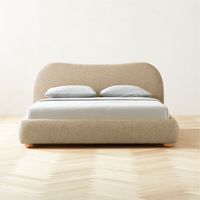 Say it with us: all-over boucle. Soft camel boucle bed designed by Los Angeles-based Ross Cassidy is reminiscent of 1930s Italy with its shapely curves and cloud-like presence. A subtle nod to traditional camel-back silhouettes with a dose of Ross' signature flair. The design is finished with solid honey oak round legs. CB2 exclusive.  -Designed by Ross Cassidy -Engineered wood frame -Wool-poly blend boucle upholstery -Solid honey oak legs -Characteristics of wood include variation in tone, natu