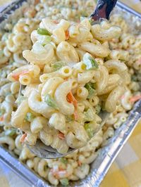 Close up serving spoon full of the best macaroni salad with celery, green peppers and shredded carrots