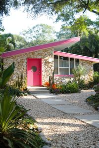 Mid-century modern house with a pink door and stone facade. Get ready for a sun-soaked adventure in Palm Springs’ mid-century marvels, where sleek design meets desert vibes and retro never looked so cool!