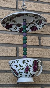 Upcycled Teacup and Saucer Bird Feeder, Purple Flowers, handmade from repurposed kitchen items. Assembled using metal fasteners (not glue). Color-coordinated wooden beads are painted with water-based, matte finish, low-VOC chalk paint safe for birds. Hang outdoors in a protected area where you can give the birds a small treat preventing them from becoming dependent on you for their food. Or hang it indoors as home decor... makes a great place to hide your candy... or add an air plant or artifici