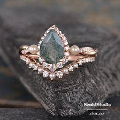 a close up of a ring with pearls and a green stone on the side, sitting on a rock