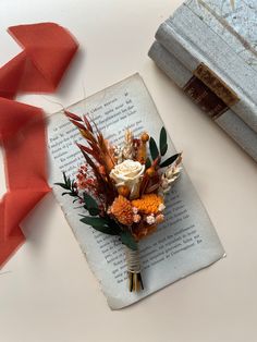 a bouquet of flowers sitting on top of an open book next to a red ribbon