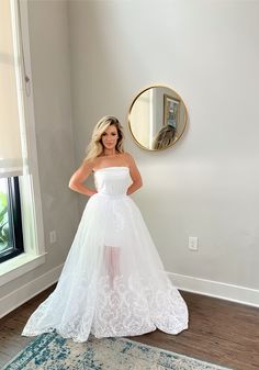 a woman in a white wedding dress standing next to a mirror and looking at the camera