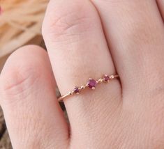 a woman's hand wearing a gold ring with three pink stones on the band