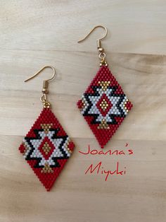 a pair of red and black beaded earrings with gold accents sitting on top of a wooden table