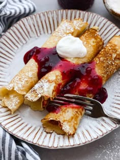 crepes with blueberry sauce and whipped cream are on a plate, ready to be eaten