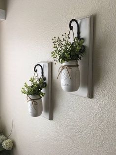 two mason jars with plants hanging on the wall