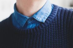 a close up of a person wearing a blue sweater and black shirt with his eyes closed