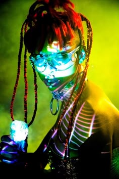 a woman with neon makeup and dreadlocks holding a light up bottle in her hand