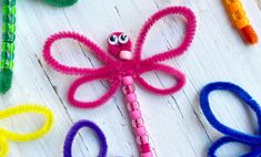 colorful hair clips with googly eyes are arranged in the shape of a dragon on a white wooden surface