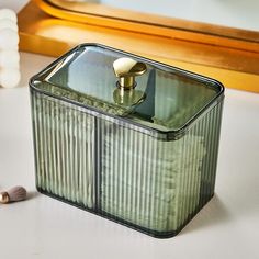 a green glass container sitting on top of a white table next to a gold framed mirror