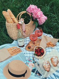 a picnic with straw hat, wine and food on the blanket in front of pink carnations