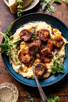 a blue plate topped with mashed potatoes and fried scallops covered in herbs