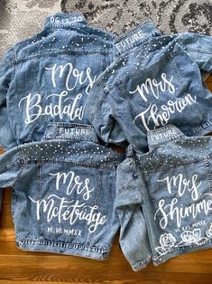 three personalized denim jackets with white writing on them sitting on top of a wooden table