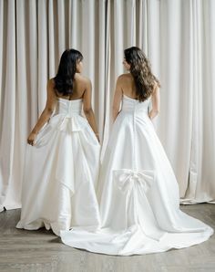 two women in white dresses standing next to each other with their backs turned towards the camera