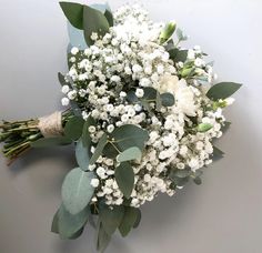 a bouquet of white flowers and greenery on a table with grey walls in the background