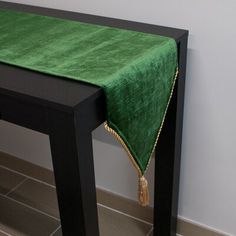 a green table cloth on top of a black table with a gold tasseled edge