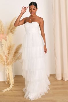 a woman standing in front of a plant wearing a white dress with tiered layers