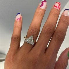 a woman's hand with colorful nail polish and an unusual ring on her finger