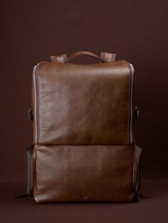 a brown leather backpack sitting on top of a brown floor next to a black wall