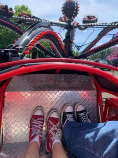 two people sitting in the back of a red car with their feet on the ground