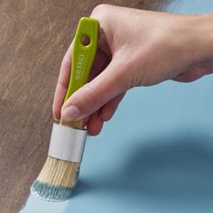 a hand holding a paint brush on top of a wooden floor with blue and white walls