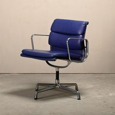 a blue leather office chair sitting on top of a cement floor next to a wall