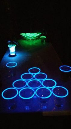 glow in the dark beer pong tables with cups on them, lit up at night