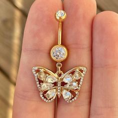 a gold colored butterfly belly button ring with clear stones on the bottom and an attached navel bar